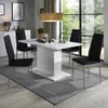 A modern dining room with a white high-gloss table and four black chairs, set against a large window with a view of greenery. Produktbild-Vorschau