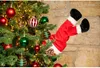 Santa's legs are stuck in a Christmas tree, decorated with ornaments and lights. Produktbild-Vorschau