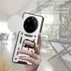 A hand holding a silver phone case with a camera cover and a ring holder, with a blurred background of an indoor setting. Produktbild-Vorschau