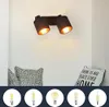 A wall-mounted light fixture with two adjustable spotlights, shown above two decorative pillows. Below the fixture are five different LED light bulbs displayed in circular frames. Voir les images du produit