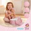 A young girl is happily holding a baby doll and a doll accessory set. Produktbild-Vorschau
