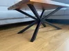 A close-up of a table leg with a wooden tabletop and a grey sofa in the background. Anteprima dell’immagine prodotto