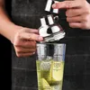 A person is assembling a cocktail shaker set, with the shaker top being placed onto a glass that has cocktail recipes printed on it. Produktbild-Vorschau