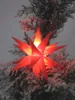 A red star-shaped Christmas light decoration is placed on a snow-covered evergreen tree. Produktbild-Vorschau