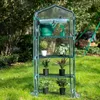 A transparent greenhouse with shelves and plants inside, placed on a grassy lawn. Produktbild-Vorschau