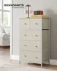A beige fabric dresser with 5 drawers stands in a well-lit room next to a doorway and a couch. A pair of headphones and a vintage-style radio are on top. Náhled obrázku produktu