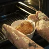 Hands wearing oven mitts are placing a netted roast into a white bowl inside an oven. Produktbild-Vorschau