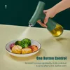 A hand holds a green oil sprayer over a plate of food, spraying oil. Podgląd zdjęcia produktu