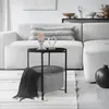 A modern living room scene with a white sectional sofa, a black side table with a basket and blanket, and decorative items on a shelf. Náhled obrázku produktu