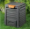 A black compost bin with orange accents sits on a green lawn, surrounded by lush green foliage. Náhled obrázku produktu