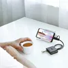 A person's hands are holding a white mug of tea on a white table, with a smartphone charging on a stand in the background. Náhled obrázku produktu