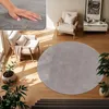 A circular gray rug is placed on a wooden floor in a living room setting, with a chair and plants. Produktbild-Vorschau