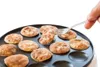 A hand is using a fork to pick up a mini pancake from a poffertjes maker. Anteprima dell’immagine prodotto