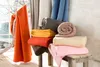 A collection of folded and rolled blankets in various colors, displayed in a cozy setting with natural light coming from a window. Produktbild-Vorschau
