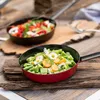 Two pans of food are displayed on a wooden surface. The front pan contains green beans, sliced apricots, and small white flowers. The back pan contains a mix of chopped vegetables including red bell peppers, celery, and mushrooms. Produktbild-Vorschau
