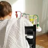 A baby is sitting in a high chair, covered by a white muslin cloth, and playing with a bead maze toy. Produktbild-Vorschau