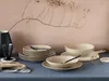 A table setting with plates, bowls, and a glass, arranged on a blue tablecloth with a pink wall in the background. Náhľad obrázku produktu