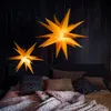 Two illuminated star-shaped lamps hang above a bed with pillows and a patterned duvet. Produktbild-Vorschau