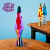 Three lava lamps are displayed on a wooden table against a light blue background. The largest lamp in the foreground has red lava in a purple liquid and a rainbow-colored base. Two smaller lamps are in the background, one with yellow and red lava, and anot Podgląd zdjęcia produktu