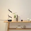 A black spiral LED desk lamp is displayed on a wooden shelf next to a potted plant and books. Podgląd zdjęcia produktu