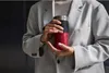 A person in a light gray blazer holds a red portable blender. Voir les images du produit