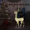 A lit-up acrylic reindeer decoration stands next to a Christmas tree with gifts underneath. Podgląd zdjęcia produktu