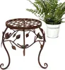 A metal plant stand with a decorative bird and leaf design, next to a potted fern in a metal bucket. Produktbild-Vorschau