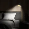 A bedside lamp illuminates a bed with a white pillow and gray blanket. Produktbild-Vorschau