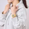 A person wearing a grey hoodie and a gold digital watch. Produktbild-Vorschau