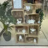 A display of wooden crates filled with decorative items, including ceramic animals and teapots, in a retail setting. Náhled obrázku produktu