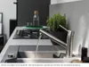 A modern kitchen sink with a faucet running water into it, a stovetop and a potted plant in the background. Anteprima dell’immagine prodotto