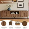 A long, wooden TV stand with a textured front, displayed in a room setting with decorative items and framed pictures on the wall. Close-up details of the product's texture and design are shown in circular insets at the bottom. Anteprima dell’immagine prodotto