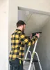 A man is standing on a ladder and holding a tool. Podgląd zdjęcia produktu