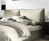 A close-up view of a bed with a beige upholstered headboard and bedding. Produktbild-Vorschau