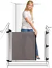 A woman is demonstrating a retractable baby gate installed at the top of a staircase. Náhľad obrázku produktu