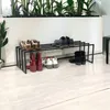 A shoe rack with various shoes on it, placed in front of a white wall with plants in the background. Podgląd zdjęcia produktu