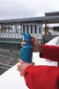 A person holding a dark blue water bottle in front of the Seattle Ferry Terminal. Produktbild-Vorschau