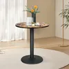 A round bistro table with a wood-look top and a black pedestal base, set on a cream rug in a room with sheer curtains and a plant. Produktbild-Vorschau