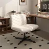 A modern home office setup with a beige office chair in the foreground, a wooden desk with a computer monitor, and bookshelves in the background.