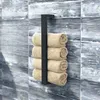 A black metal towel rack with four rolled beige towels attached, mounted on a wall with blue and gray wood-like tiles. Anteprima dell’immagine prodotto