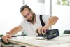A man is sanding a piece of wood with a power tool. Voir les images du produit