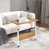A portable, height-adjustable wooden work table with wheels is placed next to a white sofa in a living room setting. Produktbild-Vorschau