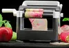 A vegetable slicer with a radish being sliced, with apples and mint leaves in the foreground. Produktbild-Vorschau