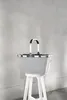 A grey reisenthel carrybag is placed on a white stool against a grey textured wall. Produktbild-Vorschau