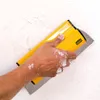 A hand is using a trowel to apply plaster to a wall. Náhled obrázku produktu