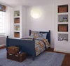 A child's bedroom with a blue bed, patterned bedding, and shelves with storage baskets and decorative items. Produktbild-Vorschau