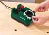 A person's hands are shown adjusting a green and gray tool on a light brown wooden surface. Produktbild-Vorschau