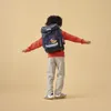 A child wearing a backpack stands with arms outstretched against a plain background. Produktbild-Vorschau