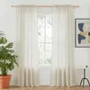 A pair of beige linen-look curtains hangs on a wooden rod in front of a window. A large potted plant is to the left, and a small side table with a framed artwork hangs on the wall to the right. Produktbild-Vorschau