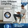 A man is reading a book while sitting on a chair next to a washing machine. Produktbild-Vorschau